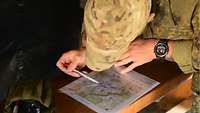 Ein Soldat hat sich tief über eine kleine Karte gebeugt. Mit einem Stift folgt er Linien auf ihr.