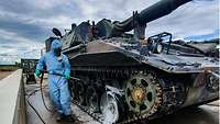 Eine Panzerhaubitze wird von einem Soldaten in Schutzkleidung eingesprüht