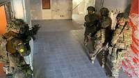 Drei US-Soldaten und ein deutscher Soldat stehen mit Gewehren im Gang vor einer Treppe