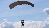 Ein Fallschirm mit zwei Soldaten an den Leinen schwebt unter bewölktem Himmel dem Boden entgegen.