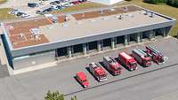 Ein großer neuer Flachbau steht auf einem noch größeren Platz. Davor stehen sechs Feuerwehr-Autos.