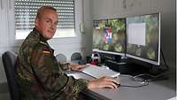 Ein Soldat sitzt am Schreibtisch vor seinem Computer. Er blickt in die Kamera.