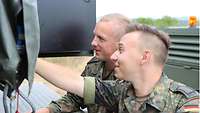 Zwei Soldaten blicken auf ein technisches Gerät. Einer der Soldaten greift hinein.