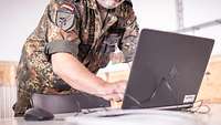 Ein Soldat steht vor einem Laptop und tippt auf der Tastatur