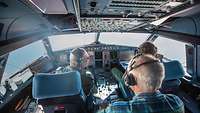 Zwei Piloten der Bundeswehr und ein Mann sitzen im Cockpit eines Airbus A321LR