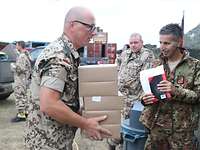 Ein Soldat trägt mehrere Verpflegungsboxen. Im Hintergrund sind weitere Soldaten zu sehen.