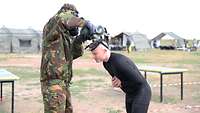 Ein Soldat in ABC-Schutzkleidung zieht einem anderen Soldaten die ABC-Schutzmaske vom Kopf.