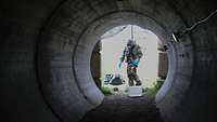 Ein Soldat in ABC-Ausrüstung schaut in ein großes Rohr aus Beton um Kampfmittel zu suchen
