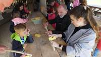 Kinder und Erwachsene versuchen sich, in einer Werkstatt des Dorfes, an Holzarbeiten.