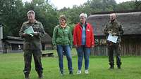 Zwei Frauen stehen auf einer Wiese, daneben stehen zwei Soldaten. Ein Soldat liest etwas vor. 