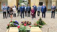 Soldaten und Zivilisten stehen an einem mit Blumen geschmückten Gedenkstein.