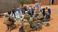 Soldaten sitzen im Wüstensand mit Einheimischen