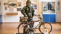 ein Wehrmachtssoldat mit seinem Fahrrad in einer Ausstellungshalle