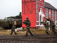 Mehrere Soldaten rennen mit Waffen im Anschlag an einem Haus vorbei.