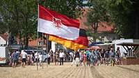 Besucher bei einer Veranstaltung im Vordergrund die Fahnen des Landes Brandenburg und Deutschlands