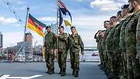 Drei Soldaten mit einer Flagge an Bord eines Schiffes mit angetretenen Soldaten an der Seite.