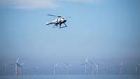 Eine graue Hubschrauberdrohne schwebt über einem Windpark in See