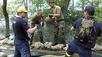 Zwei Soldaten und zwei Mitarbeiter des Technischen Hilfswerks bauen eine Deichverstärkung aus Sandsäcken