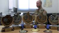 Ein Soldat sitzt an einem Schreibtisch; vor ihm sind Pokale aufgereiht