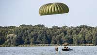Soldat mit geöffnetem Fallschirm landet im Wasser, in seiner unmittelbaren Nähe ein Boot
