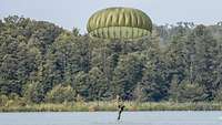 Soldat mit geöffnetem Fallschirm landet im Wasser, in seiner unmittelbaren Nähe ein Boot