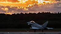 Ein spanischer Eurofighter landet in Ämari, während die untergehende Sonne die Wolken in ein goldgelbes Licht taucht.