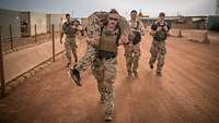 Ein Soldat trägt einen Kameraden auf den Schultern, andere folgen ihm