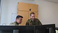 Zwei Soldaten stehen vor zwei Monitoren und betrachten einen der beiden.