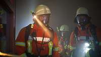 2 Feuerwehrleute mit schwerer Ausrüstung und Atemmasken im Rauch.