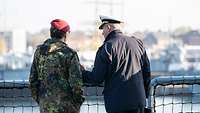 Ein Soldat der Marine und ein Heeressoldat stehen auf einem Schiff der deutschen Marine und unterhalten sich.