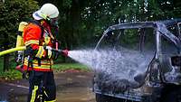 Ein Feuerwehrmann löscht die letzte Glut an einem ausgebrannten Fahrzeug.