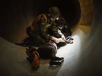 Ein Soldat und ein Polizist knien in einem dunklen Tunnel vor einem schwer verletzten Hunde-Dummy und legen eine Infusion