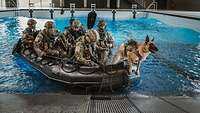 Ein Diensthund springt aus einem Schlauchboot mit mehreren Soldaten in einer Schwimmhalle während einer amphibischen Landeübung