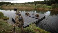 Auf einem Fluss koppeln zwei Soldaten schwarze Module zusammen. Am Ufer steht ein weiterer Soldat.