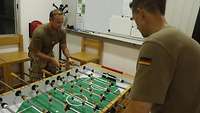 Zwei Soldaten in T-Shirts mit Deutschlandflaggen auf dem Ärmel stehen an einem Tischkicker und spielen eine Partie