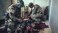 Zwei KSK-Soldaten versorgen in einem Gebäude einen am Boden liegenden Soldaten mit einer schweren Beinverletzung.