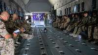 Soldatinnen und Soldaten sitzen andächtig im Frachtraum eines Militärtransportflugzeugs