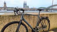 Ein Fahrrad lehnt an einer Mauer; im Hintergrund der Kölner Dom