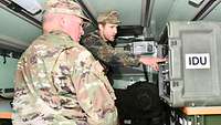 In einem militärischen Fahrzeug zeigt ein deutscher Soldat einem US-amerikanischen General Geräte.