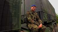 A soldier in field dress sits on a Bundeswehr truck between driver's cab and trailer.