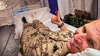Ein Soldat liegt auf einem Krankenbett. Sein Fuß ist eingegipst. Er streckt den Daumen nach oben und lächelt.