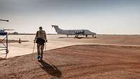 Ein Soldat geht an Krücken auf ein kleines Flugzeug zu