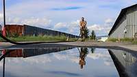Ein Soldat zieht einen Tankschlauch aus. Sein Antlitz spiegelt sich im Regenwasser.