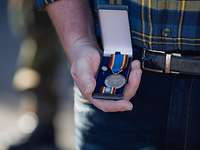 Nahaufnahme der Hand eines Zivilisten, die eine Schatulle mit Medaille, Bandschnalle und Anstecknadel hält