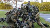 Mehrere Soldaten in grünen Uniformen trainieren ein Szenario. Dabei bereiten sie einen Kameraden für den Transport vor.