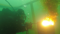 Ein Taucher hält unter Wasser eine thermische Lanze, an deren Ende entsteht eine Stichflamme.