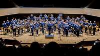 Vom Zuschauerrang geht der Blick auf die Bühne. Dort stehen rund 50 Soldatinnen und Soldaten als Orchester aufgestellt. 