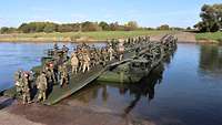 Über eine grüne militärische Behelfsbrücke laufen viele Soldaten von einem Flussufer zum anderen.