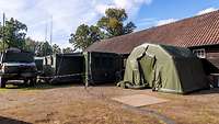 Neben einem alten Stall stehen grüne Zelte und ein getarnter Lastwagen.