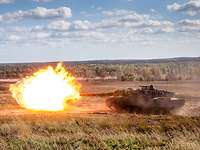 Auf weitem freien Gelände schießt ein Panzer, ein großer gelber Feuerball verlässt die Kanone.